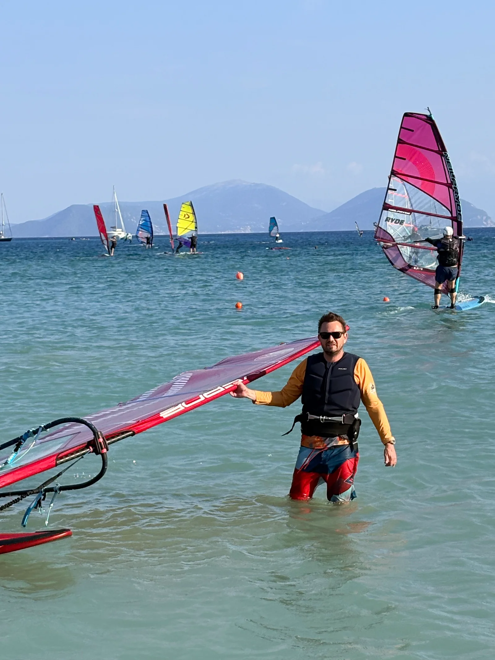 Windsurfer z żaglem w płytkiej wodzie na tle gór i zatoki